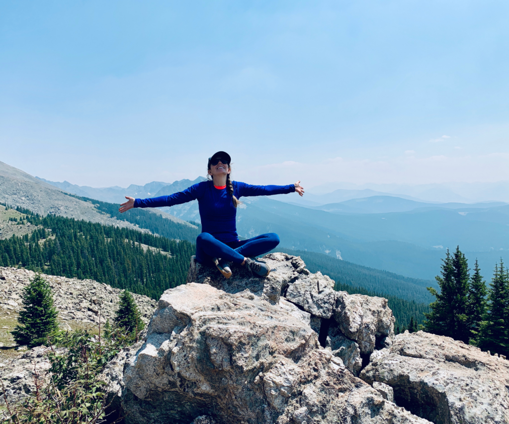 Person sitting on top of a mountain, arms outstretched 