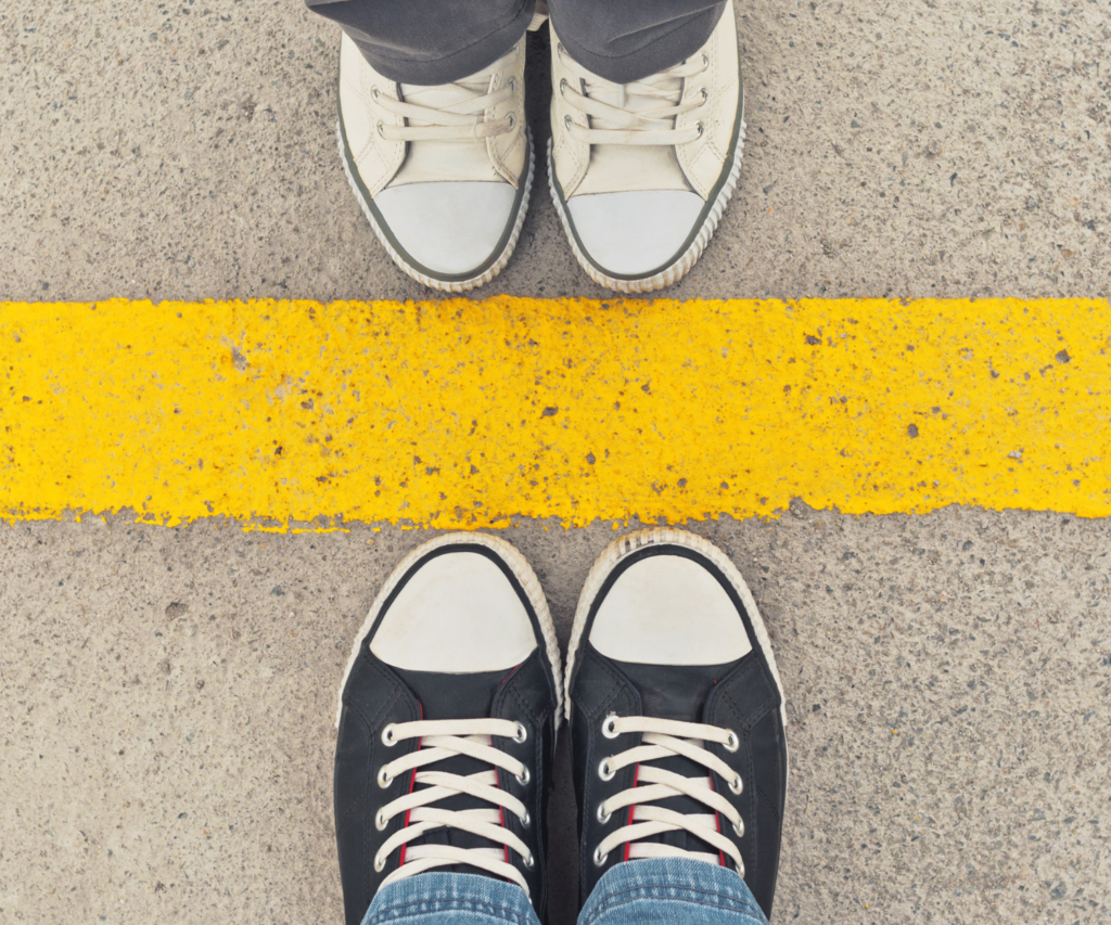 two people wearing converse shoes 
 separated by a yellow painted line on the street. 
